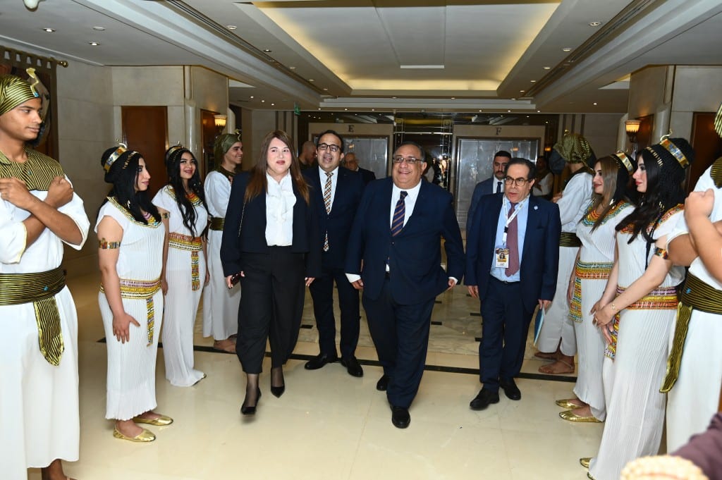 Delegates walk through a corridor lined on both sides by hosts dressed in white and gold pharaonic costume with tall headdresses.